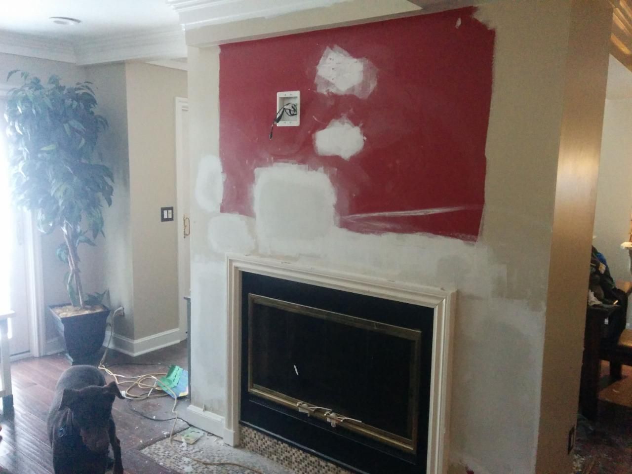 Fireplace with red painted area being patched, interior setting. Dog watches.