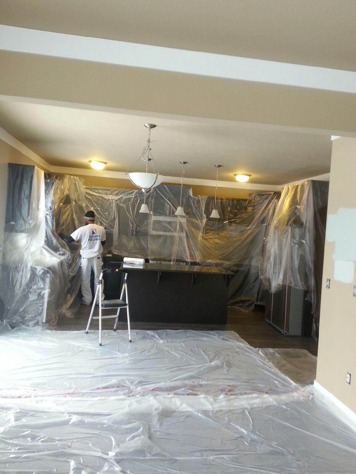Painter in a kitchen covered in plastic sheeting; painting walls.
