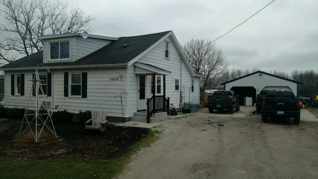 White house with black shutters and a garage, two black trucks in the driveway under an overcast sky.