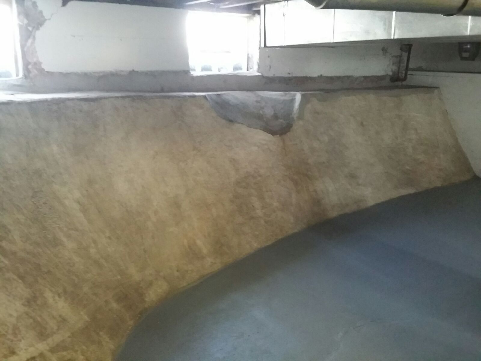 A close-up of a tan, rough-textured surface with a dark gray floor. The texture appears weathered.