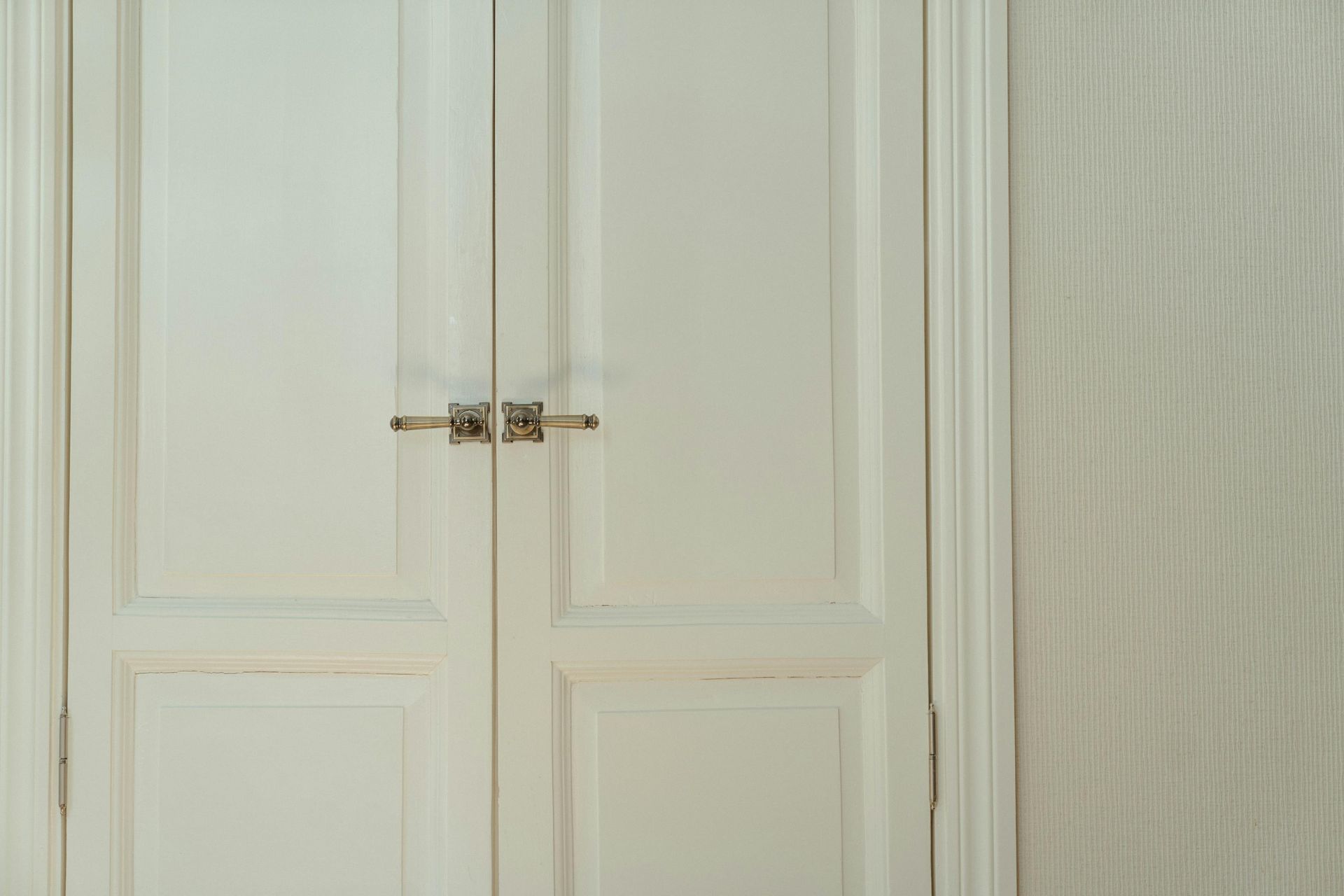 White double doors with silver hardware, set in a white door frame. A textured beige wall is on the right.