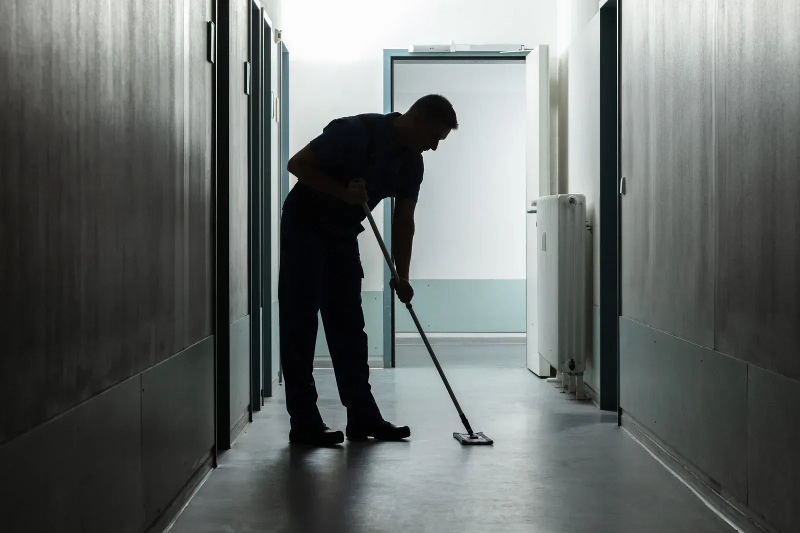 Silhouette of a person mopping a hallway floor, a janitor at work.