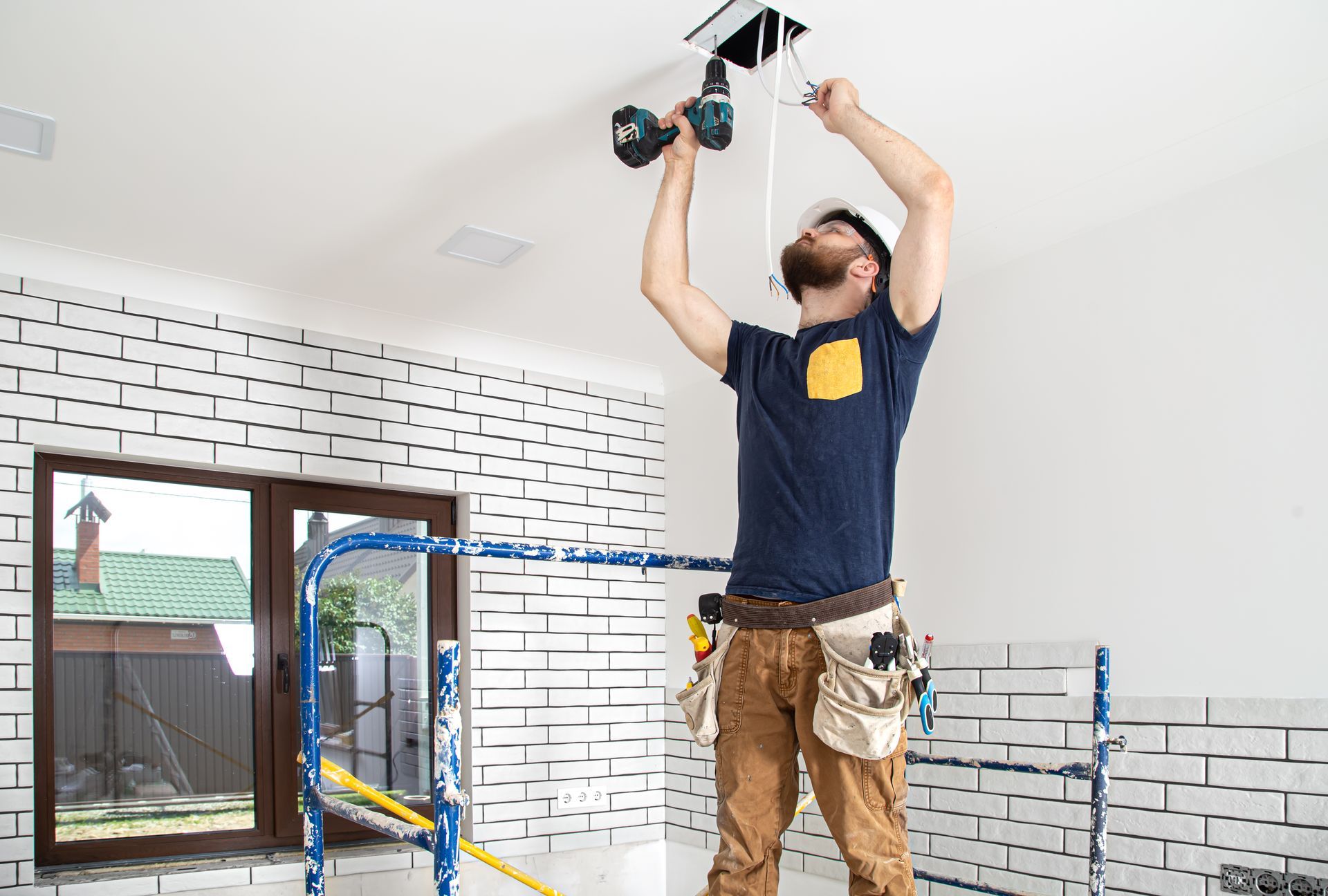 A man is using a drill to install a light fixture on the ceiling.