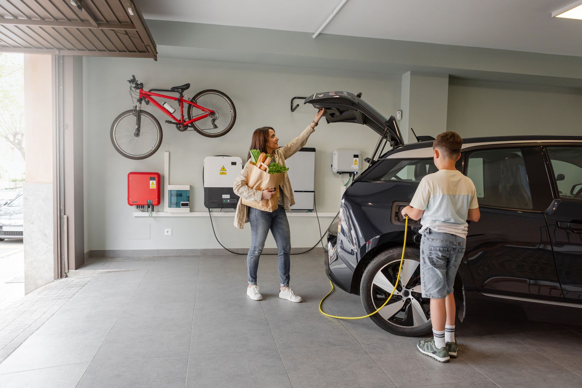 A woman and a boy are charging a car in a garage.