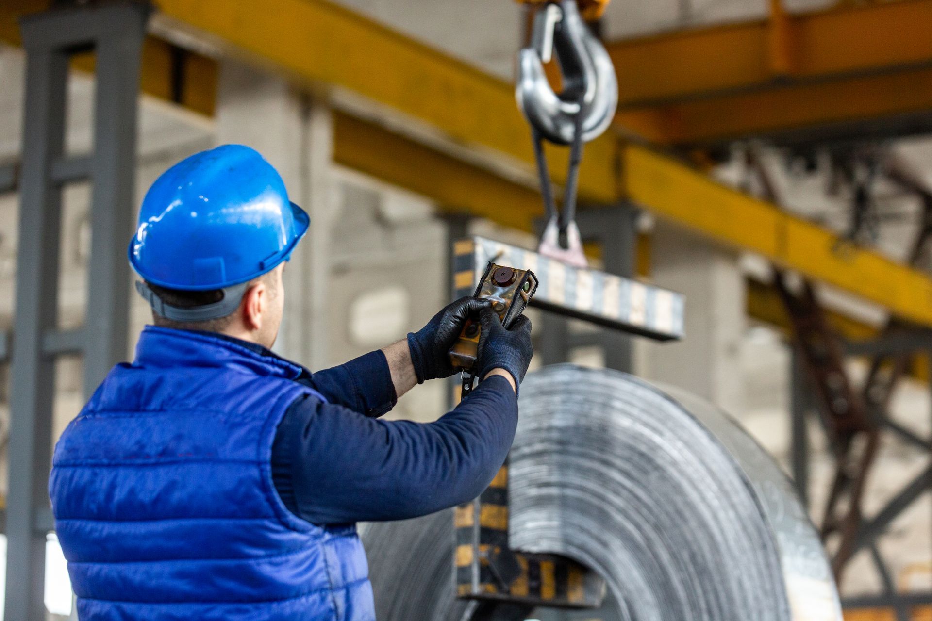 A man is lifting a large roll of metal with a crane.