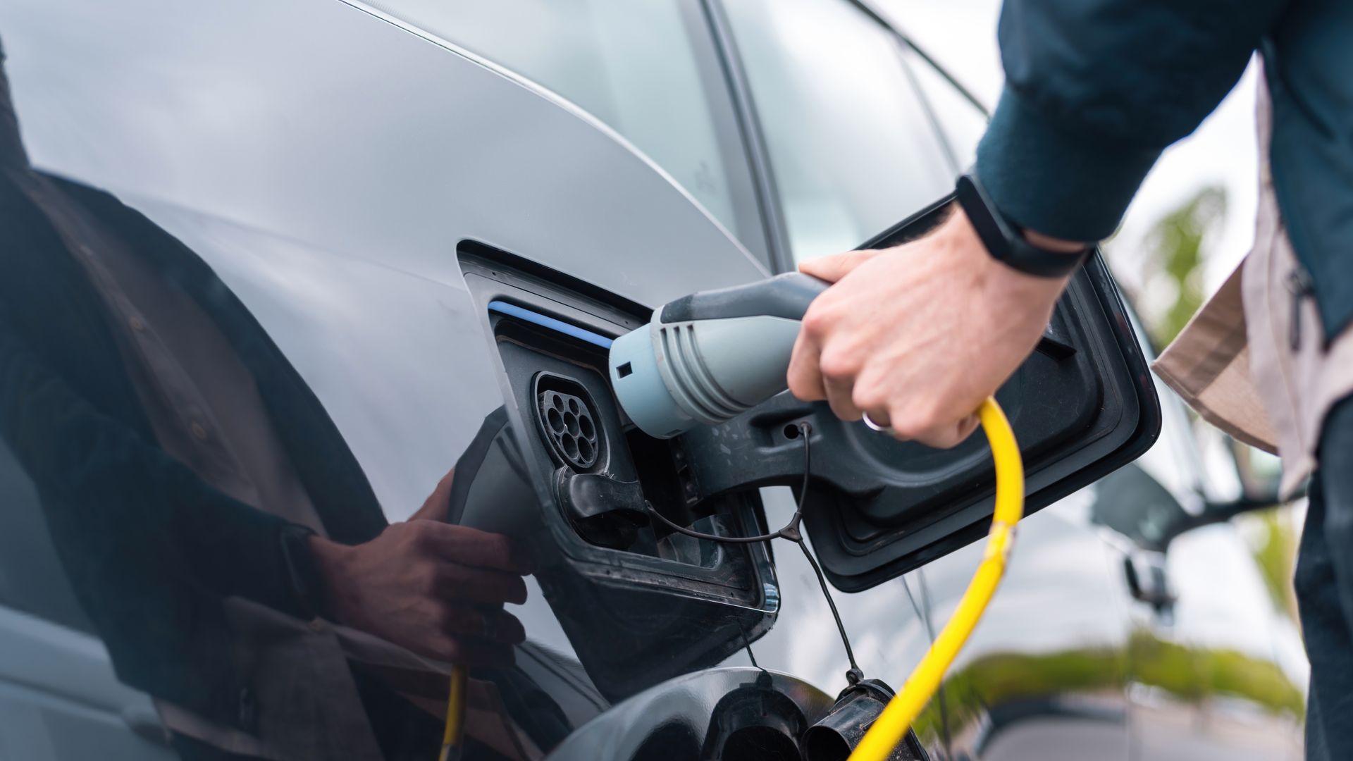 Person plugging a yellow charging cable into a black electric car.