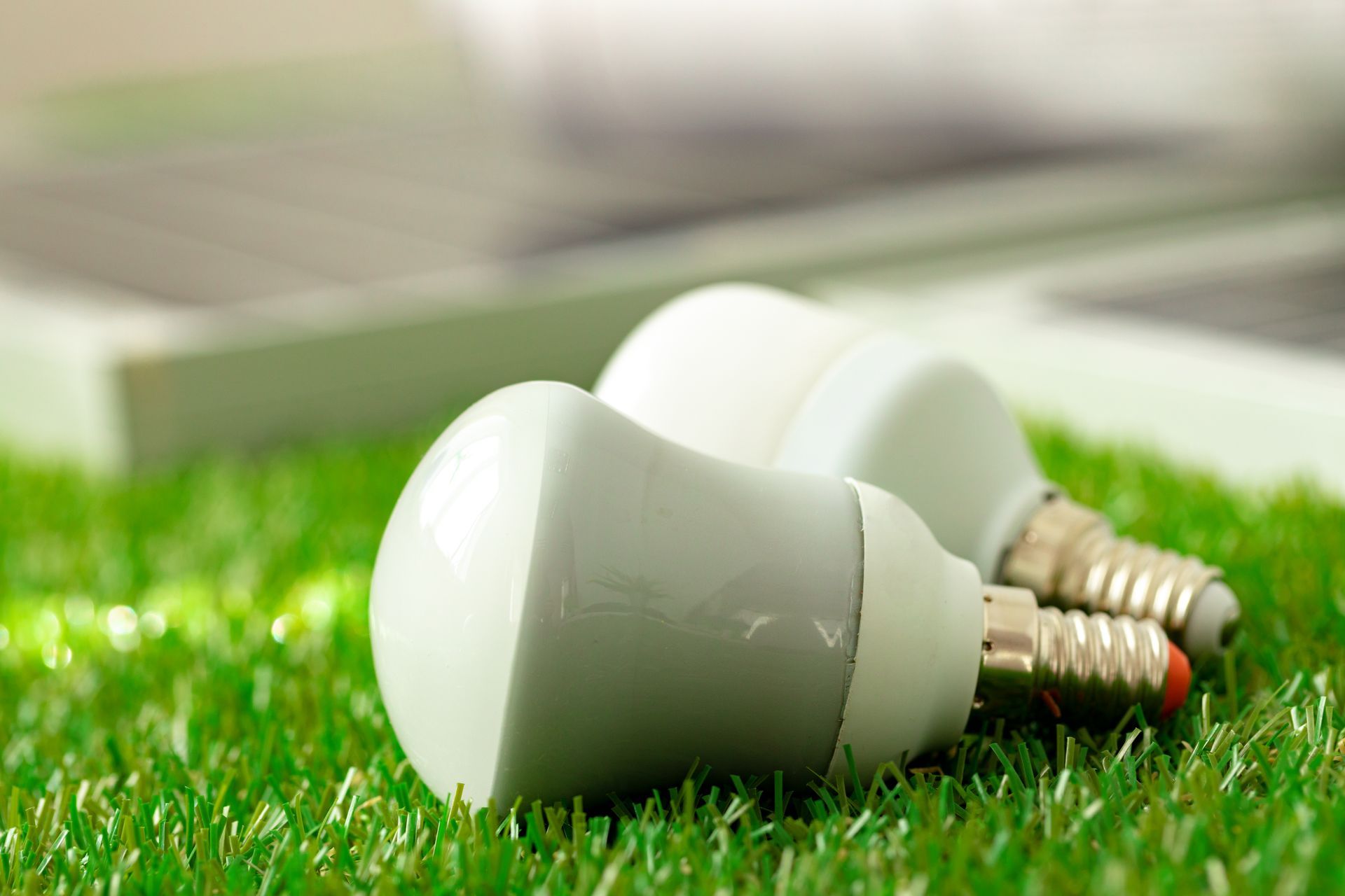 Two white LED light bulbs on green artificial turf with a blurred background.