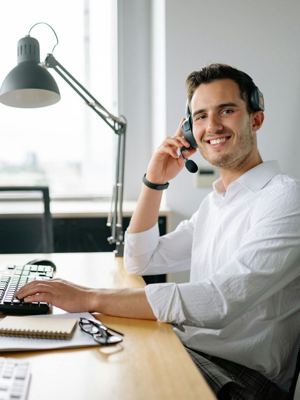 A man wearing a headset is sitting at a desk using a computer.