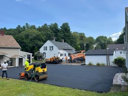 Asphalt paving project in residential area with workers operating machinery.