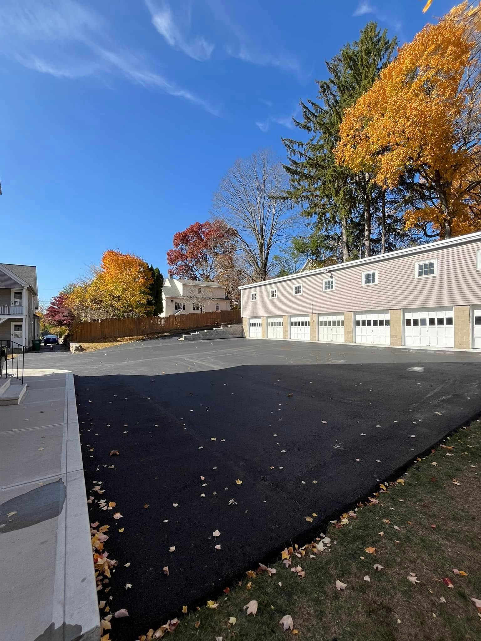 Paved lot with garages, colorful trees in the fall against a bright blue sky.