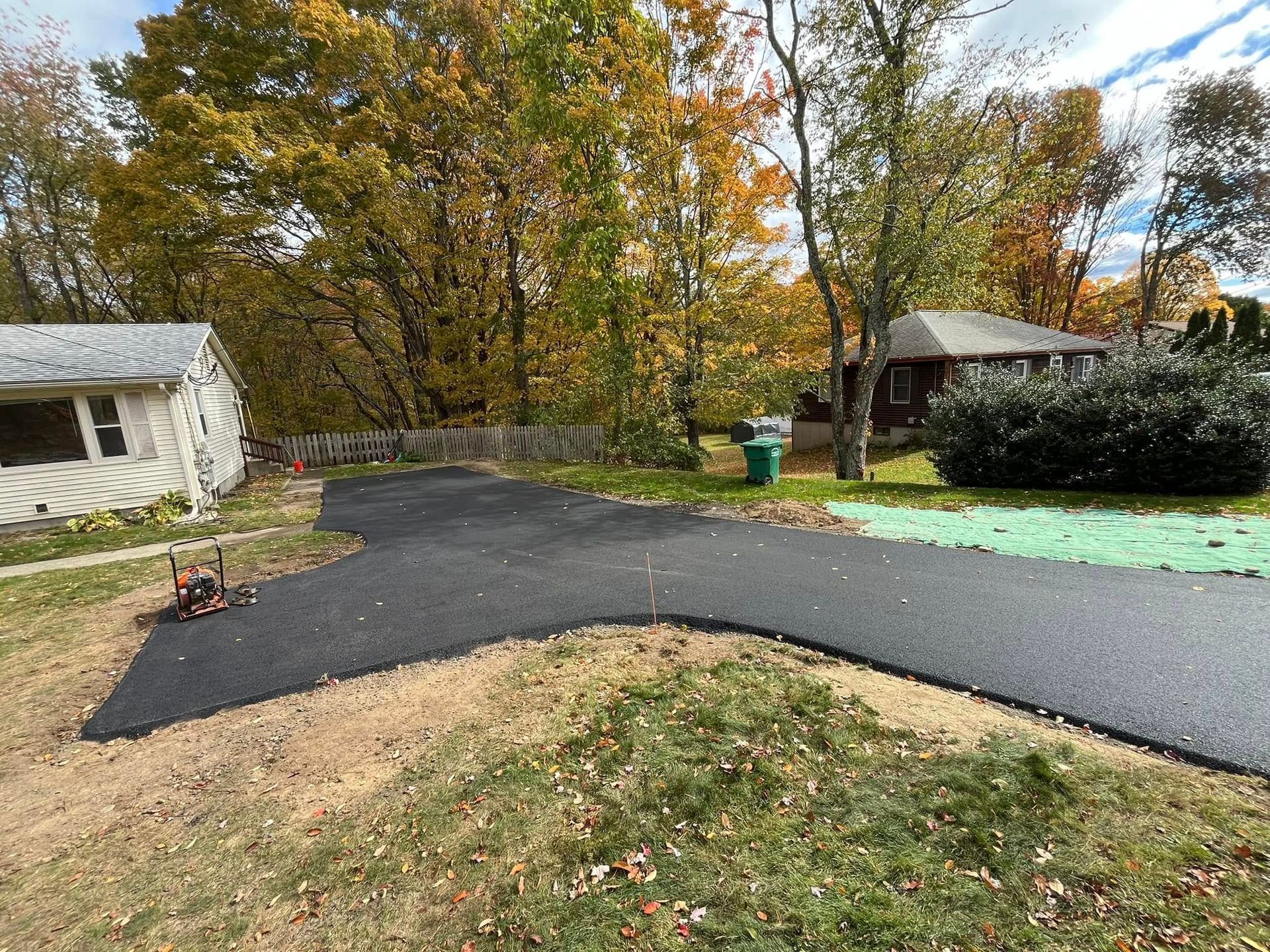 Newly paved asphalt driveway leading towards houses with fall foliage.