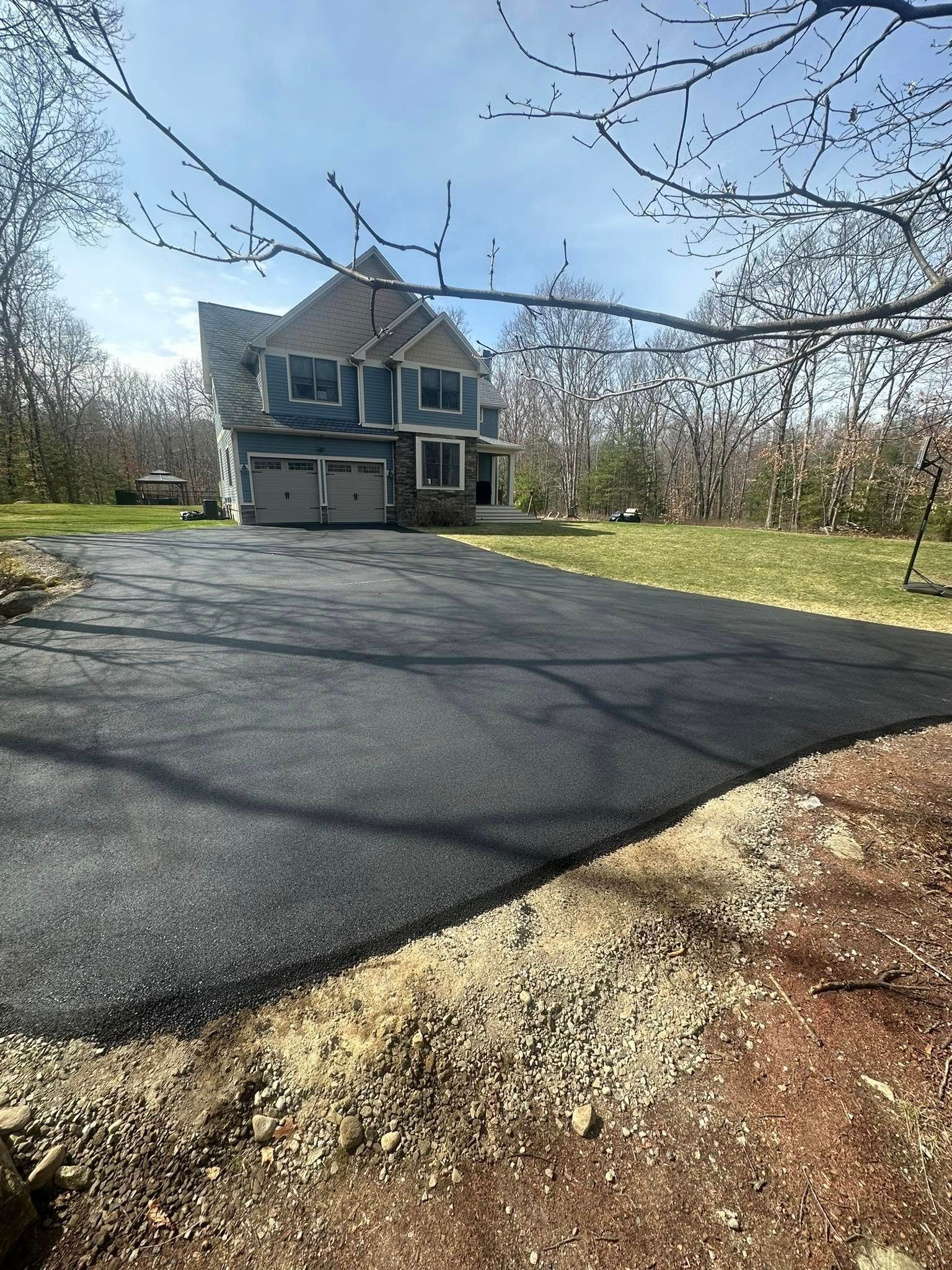 Newly paved asphalt driveway leading to a blue house with a two-car garage, sunny day.