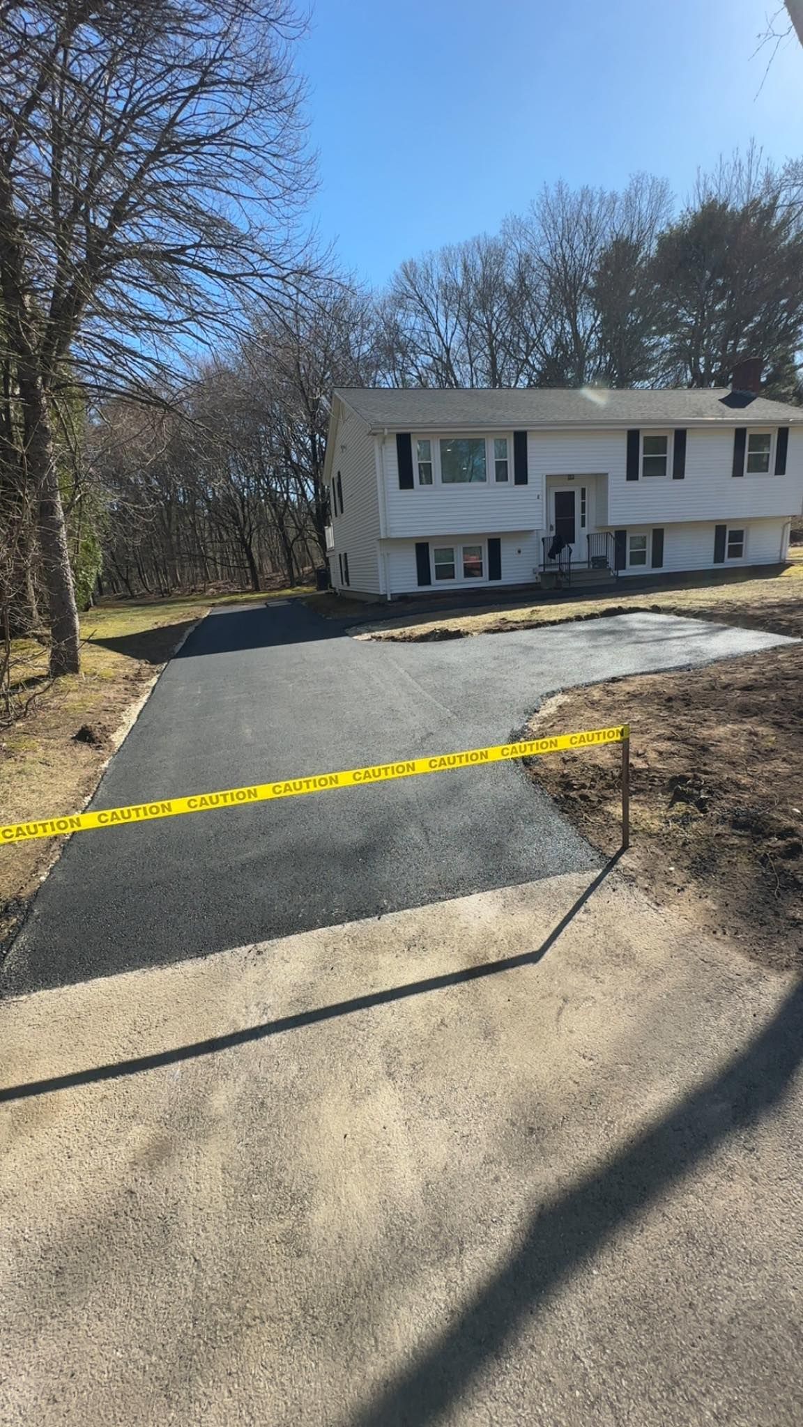Newly paved driveway leading to a two-story white house, yellow caution tape.