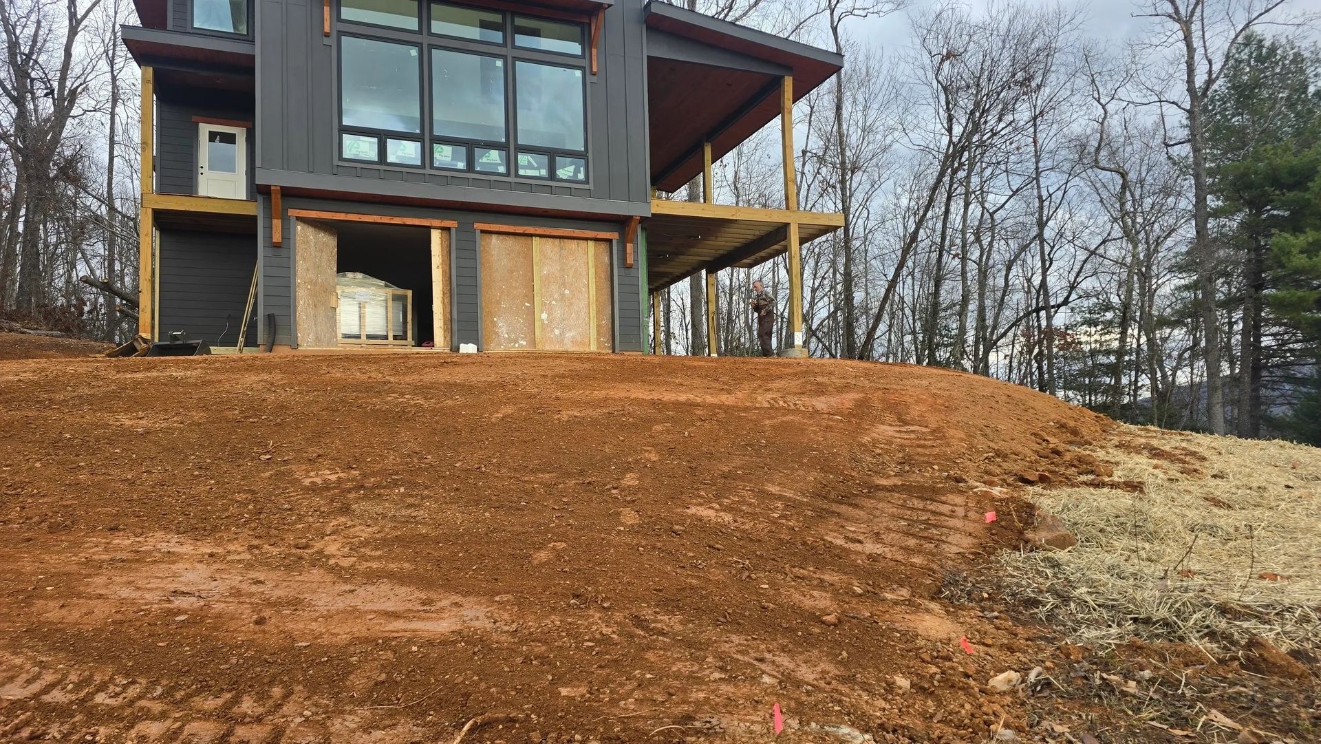 Modern house on a hillside with brown dirt and exposed foundation. Trees in the background.