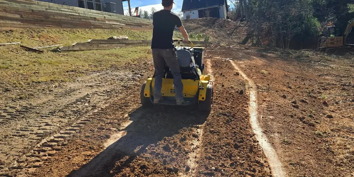 A person operating a yellow and gray compactor, creating a path in a brown field.