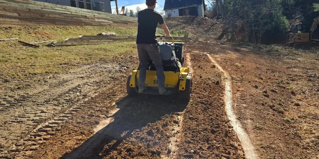 A person operating a yellow and gray compactor, creating a path in a brown field.