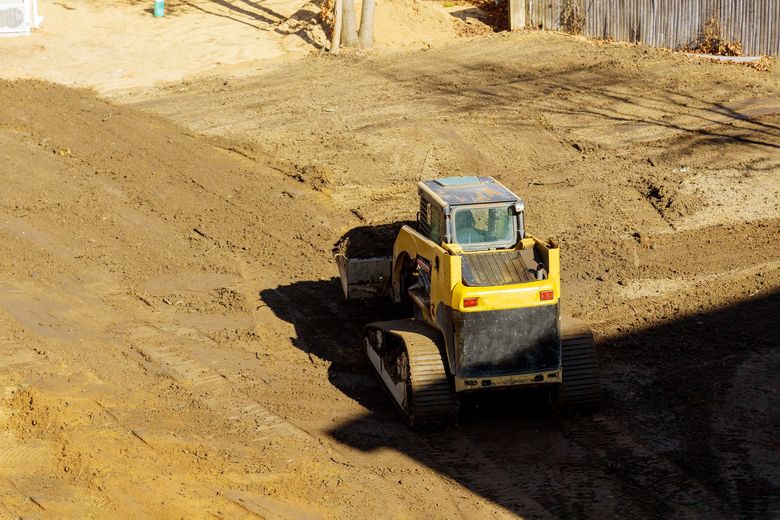 Yellow skid steer moving dirt on a construction site.