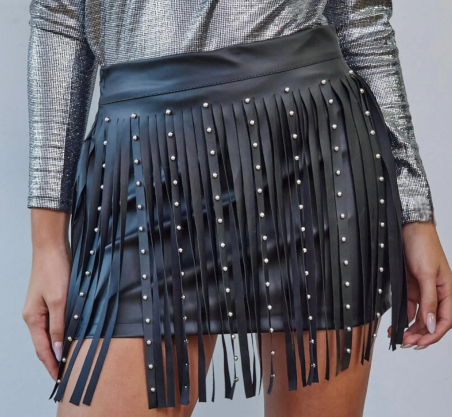 Mujer con falda de cuero negra con flecos y tachuelas plateadas; combinada con top plateado.