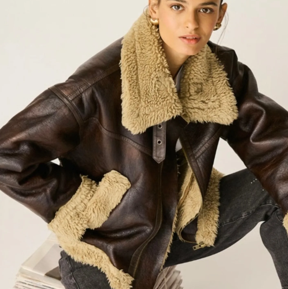 Mujer con una chaqueta de piel de oveja marrón, mirando hacia adelante, jeans oscuros, entorno de estudio.