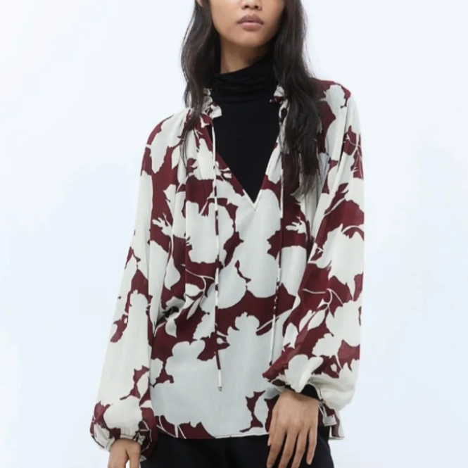 Mujer que lleva una blusa floral en color crema y granate sobre un cuello alto negro.