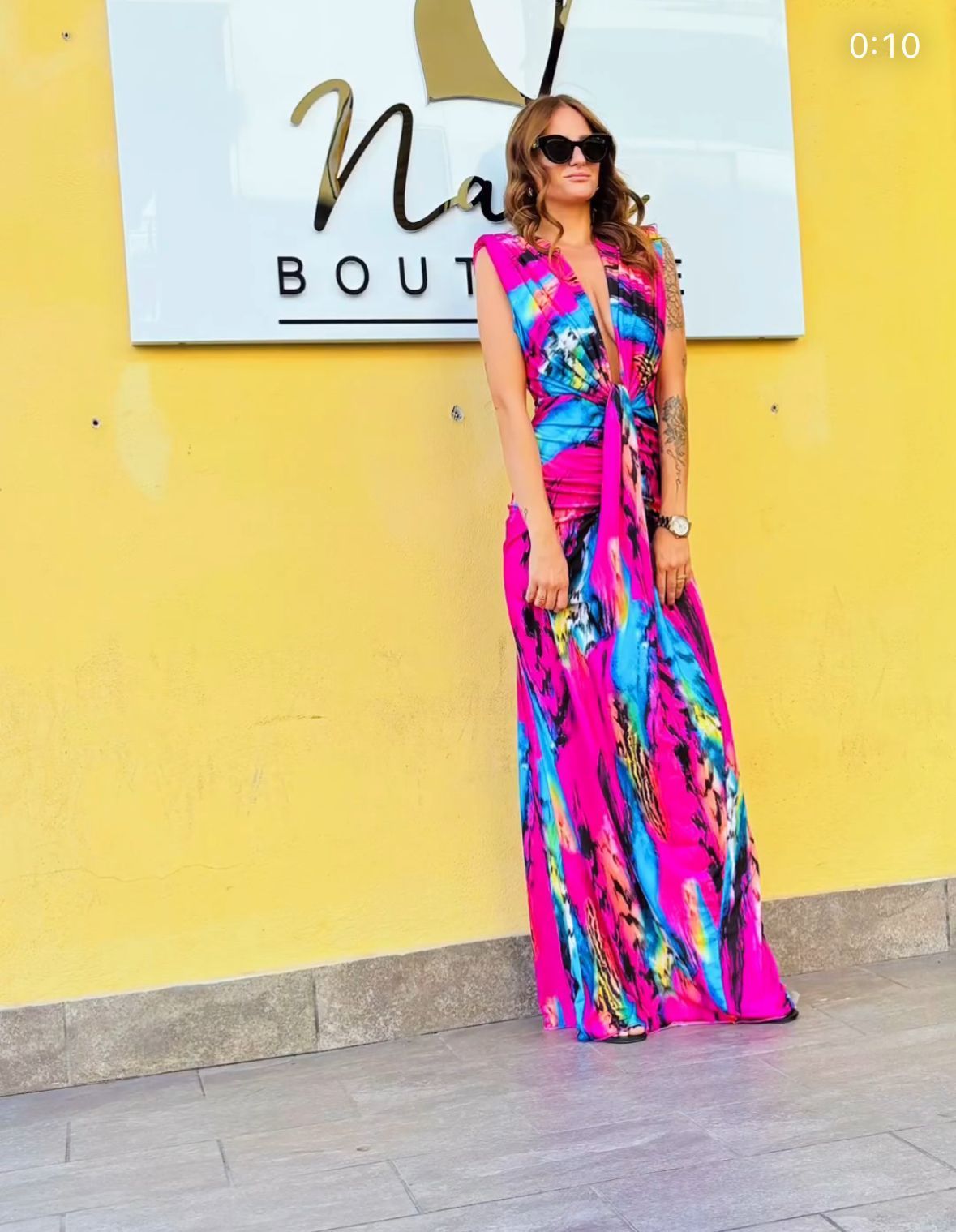 Una donna con un vestito colorato è in piedi davanti a un cartello 