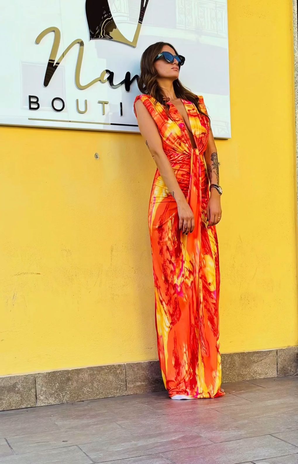 Una donna con un vestito arancione è in piedi davanti a un muro giallo.