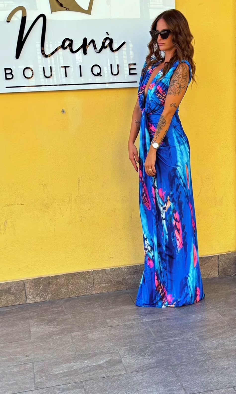 Una donna con un vestito blu è in piedi davanti al cartello di una boutique della nonna.