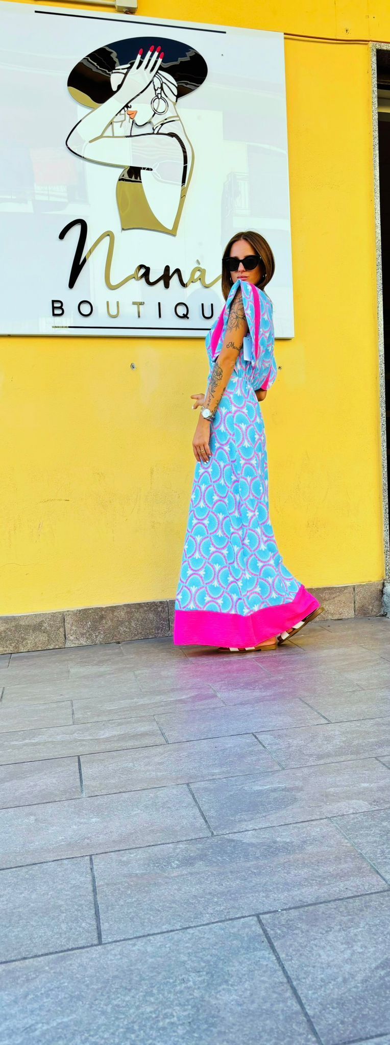 Una donna con un vestito blu e rosa è in piedi davanti a un edificio giallo