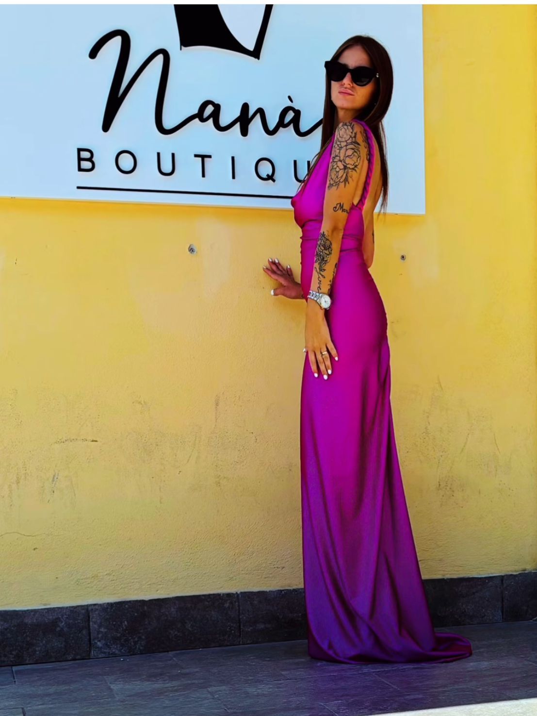 Una donna con un vestito viola sta in piedi davanti al cartello di una boutique di nana