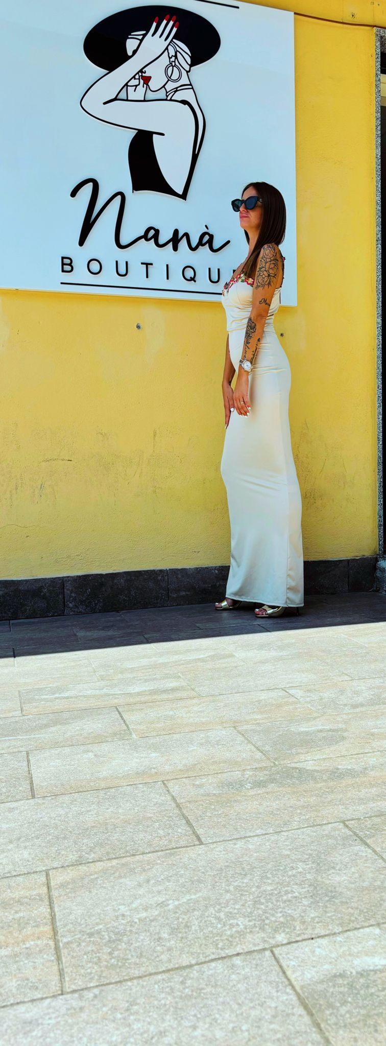 Una donna in abito bianco è in piedi davanti al cartello di una boutique di nana