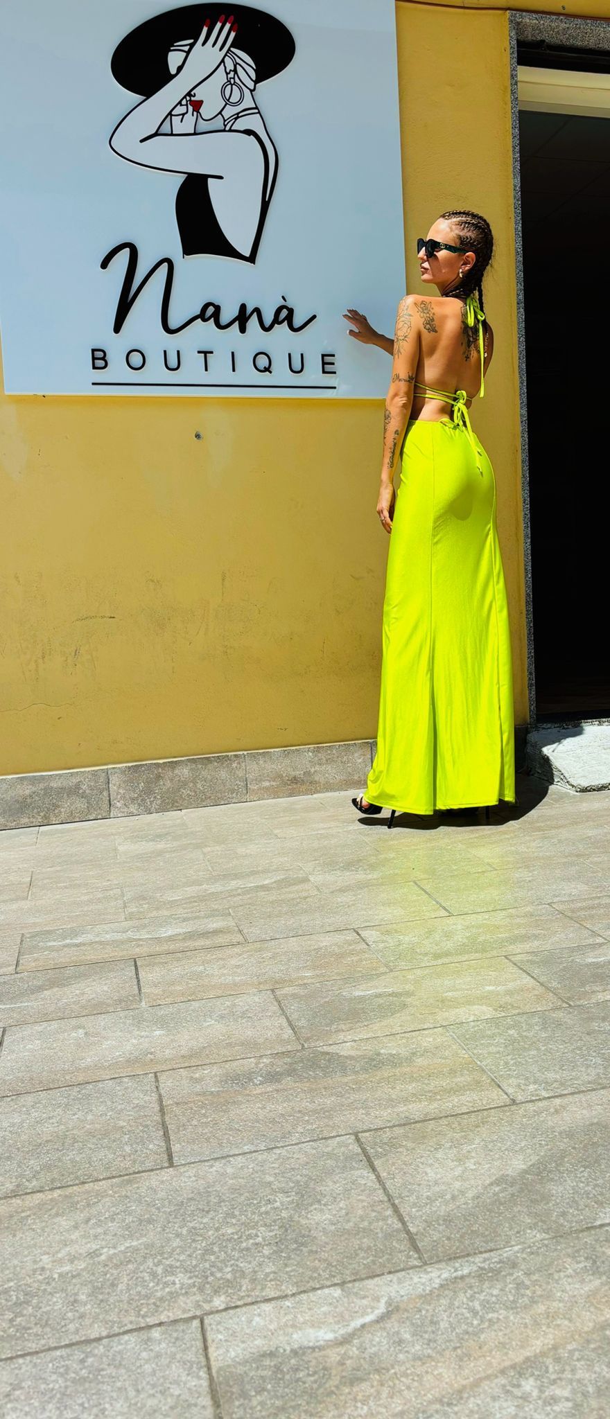 Una donna con un vestito giallo neon è in piedi davanti a un cartello.
