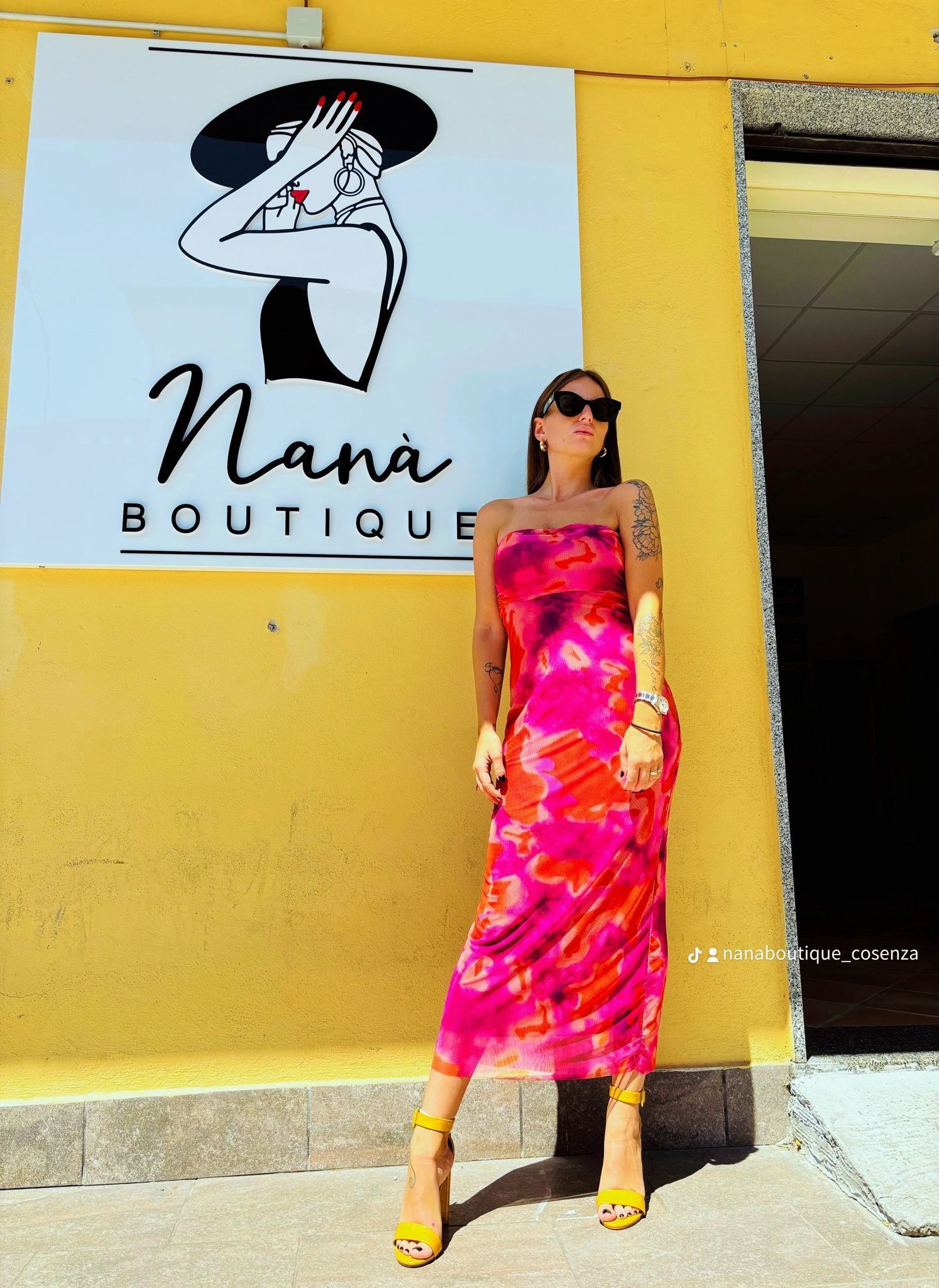 Una donna con un vestito rosa è in piedi davanti al cartello di una boutique di nana