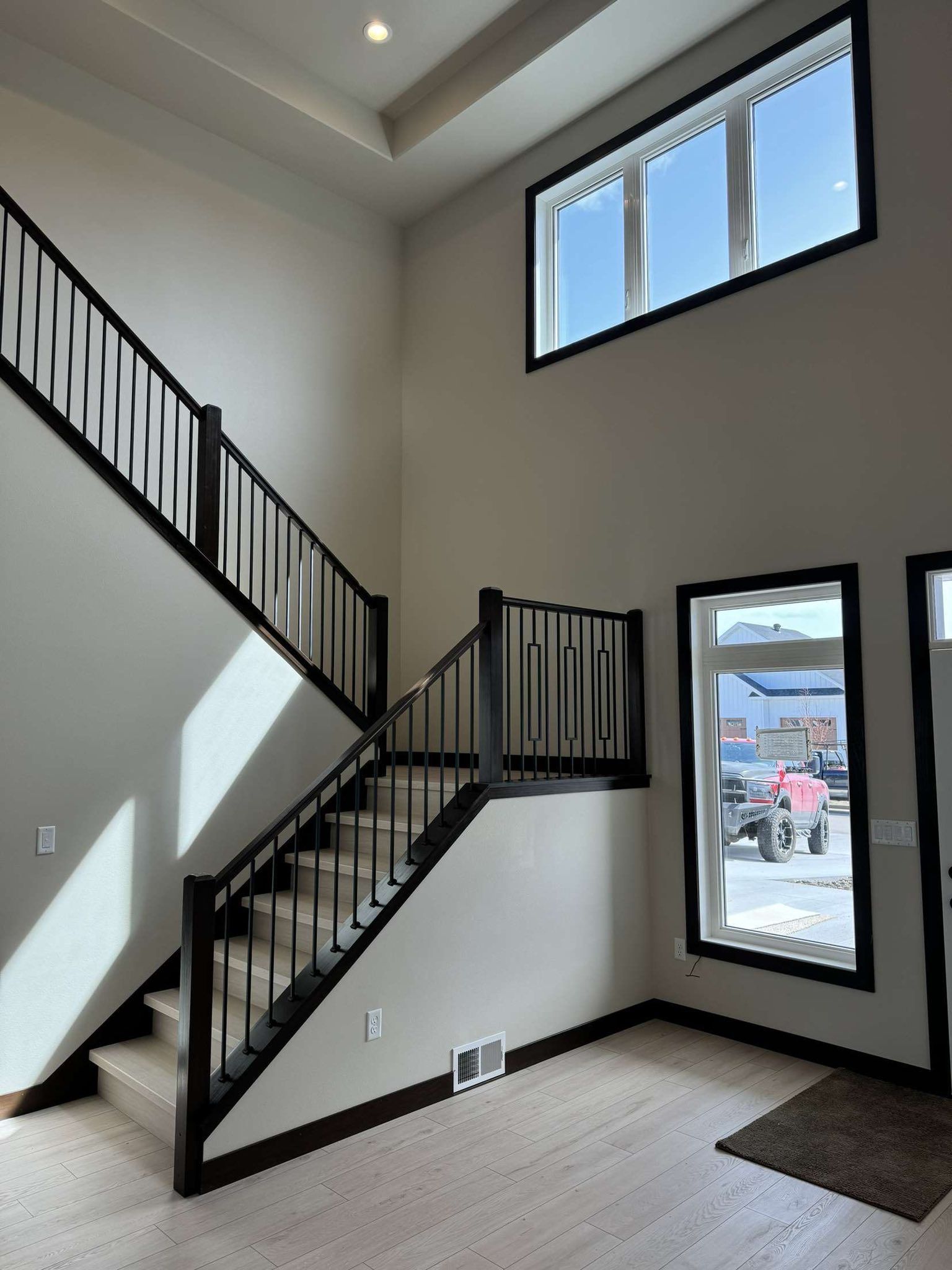 Staircase in modern house with black railing, light wood floors, two windows, and tan walls.
