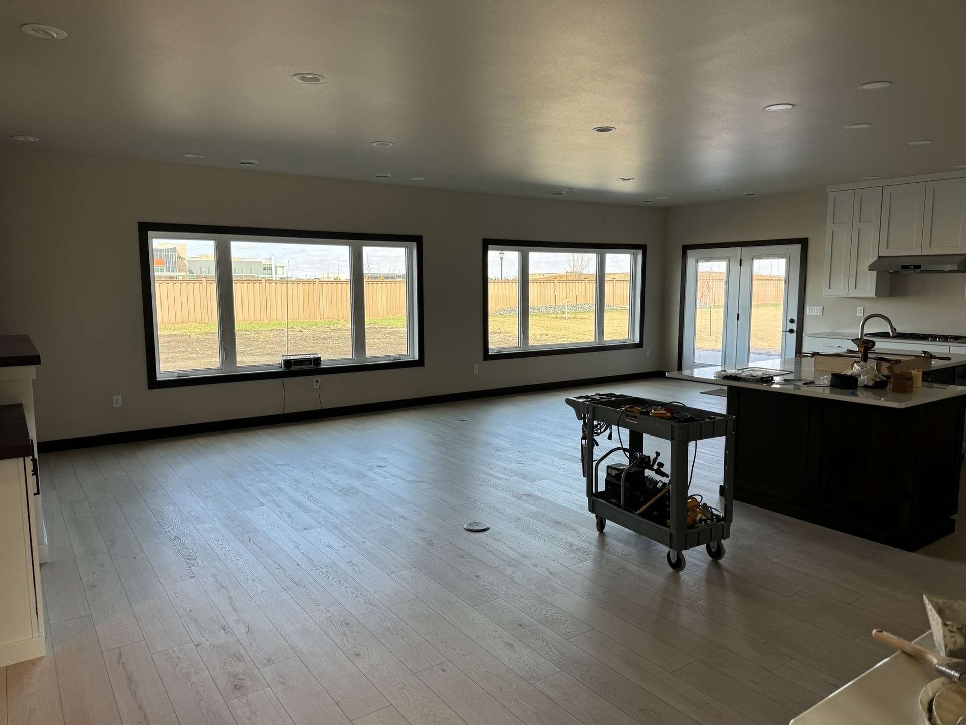 Empty living space with light wood floors, large windows, and dark trim.