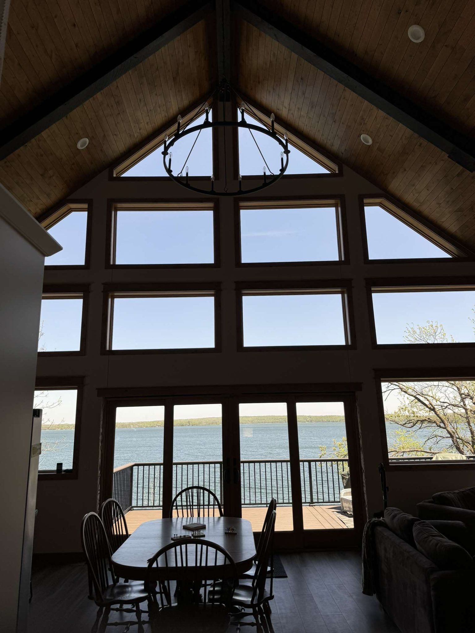 Dining room with large windows overlooking a lake. A chandelier hangs above the table and chairs.