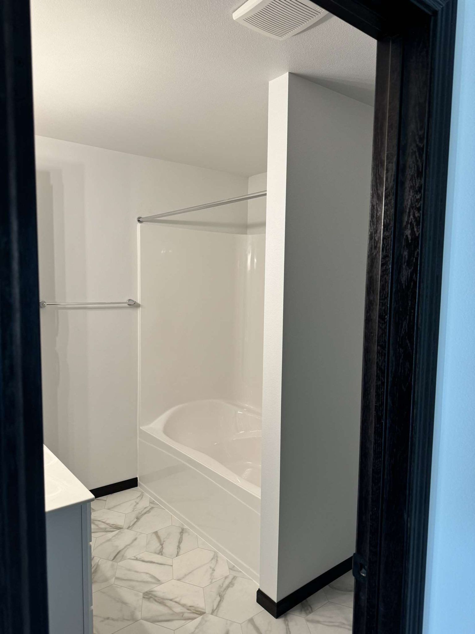 White bathroom with tub, shower, and white marble floor. Black trim around doorway.