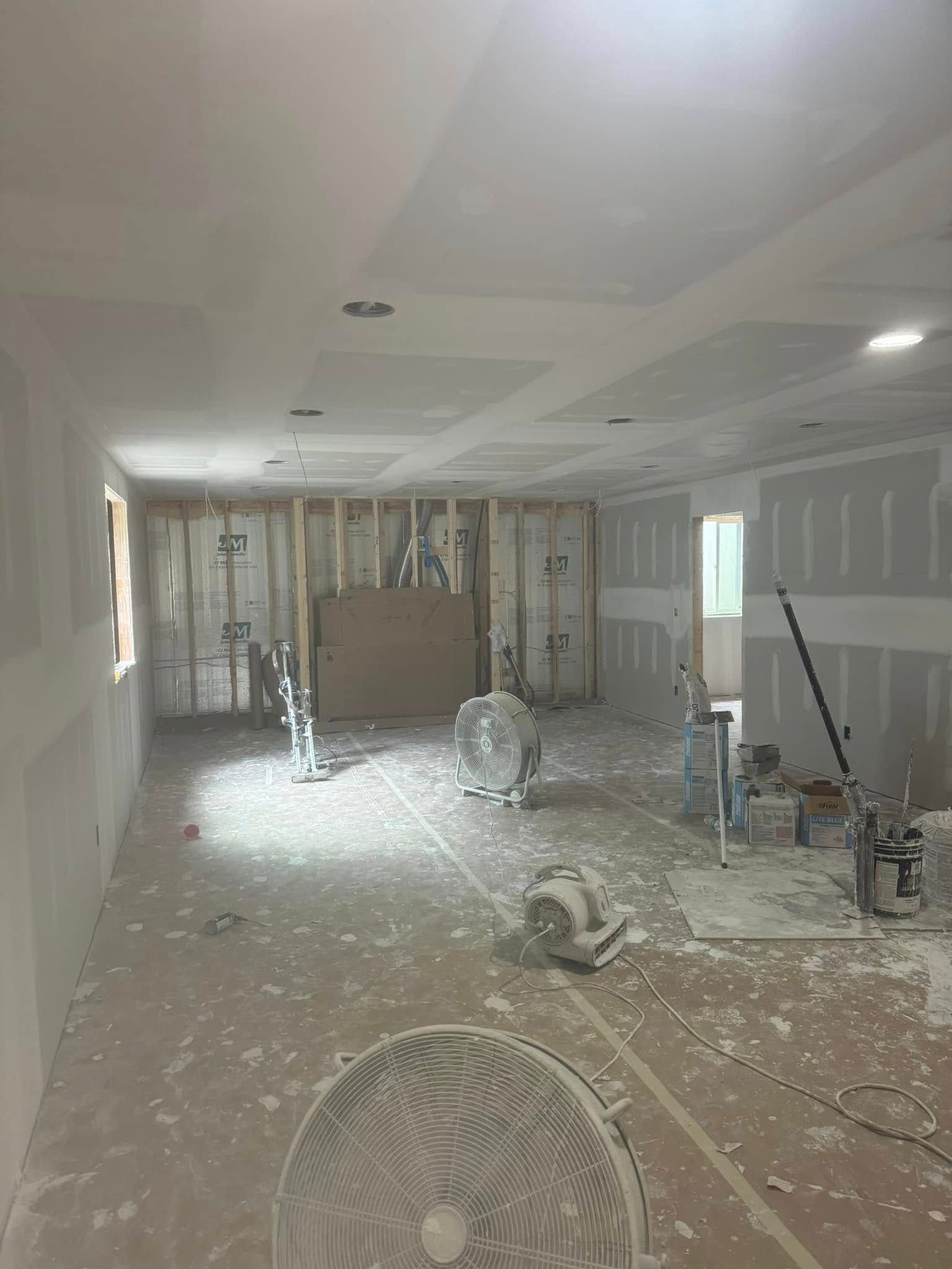 Interior room under construction, drywall installed, fans on floor, framing visible, white dust, bright.