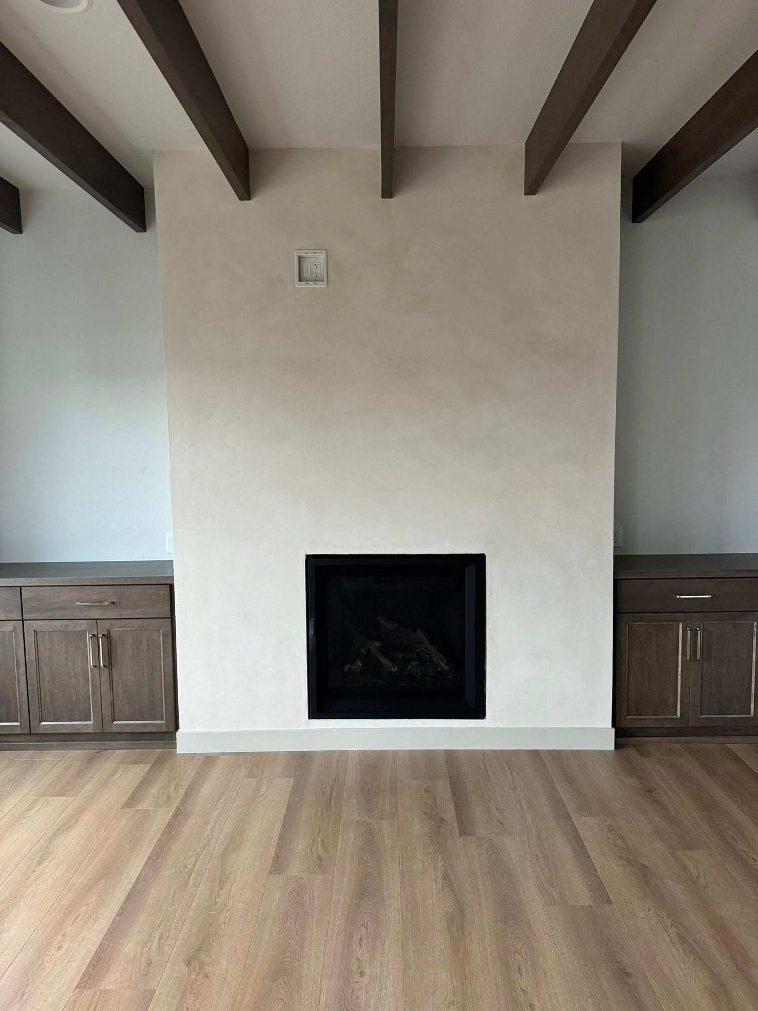 Fireplace with dark trim, white wall, and dark wood beams. Wooden cabinets flank the fireplace.