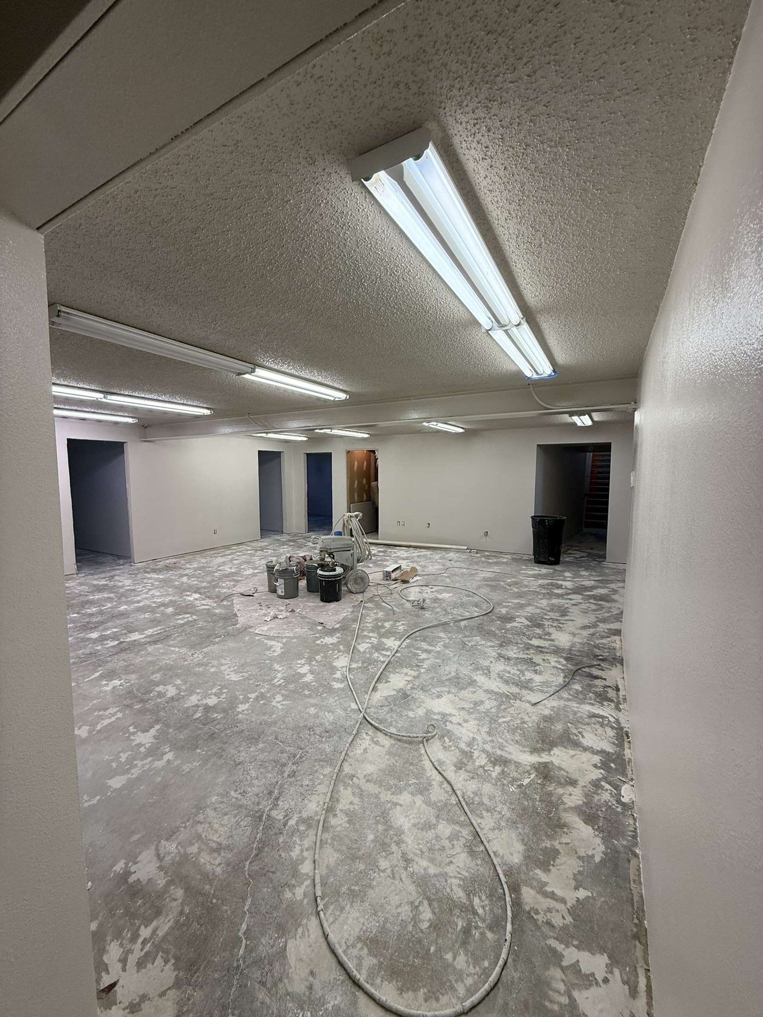 Renovated room with peeling paint, exposed concrete floor, and multiple open doorways. Fluorescent lights illuminate the space.