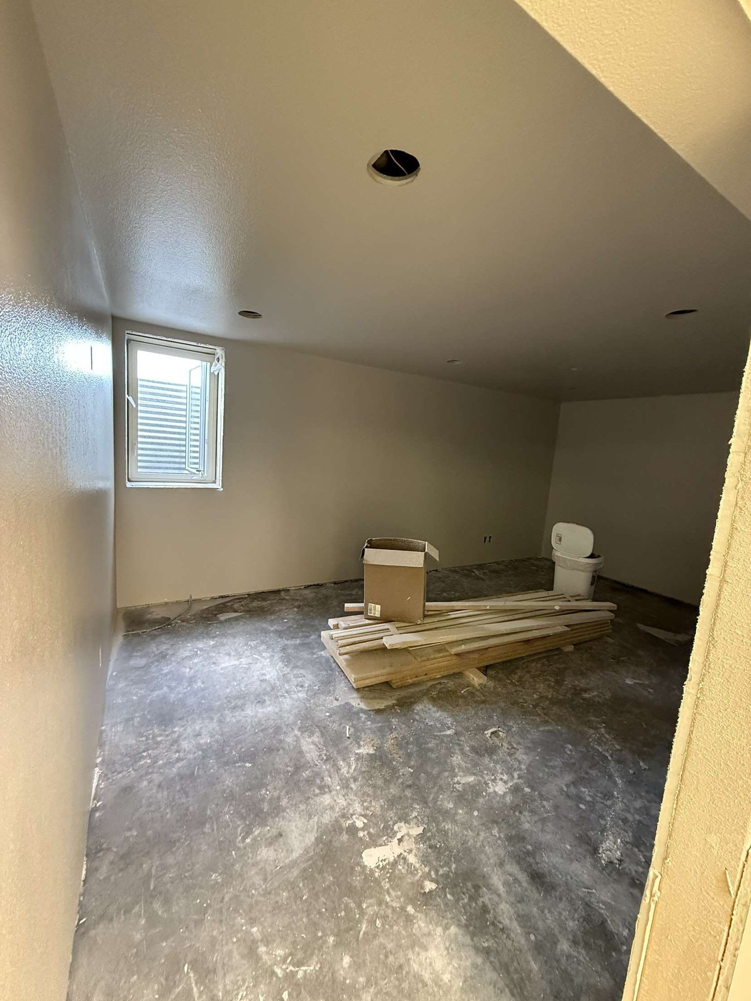 Basement room under construction with unfinished concrete floor, bare walls, and a window.