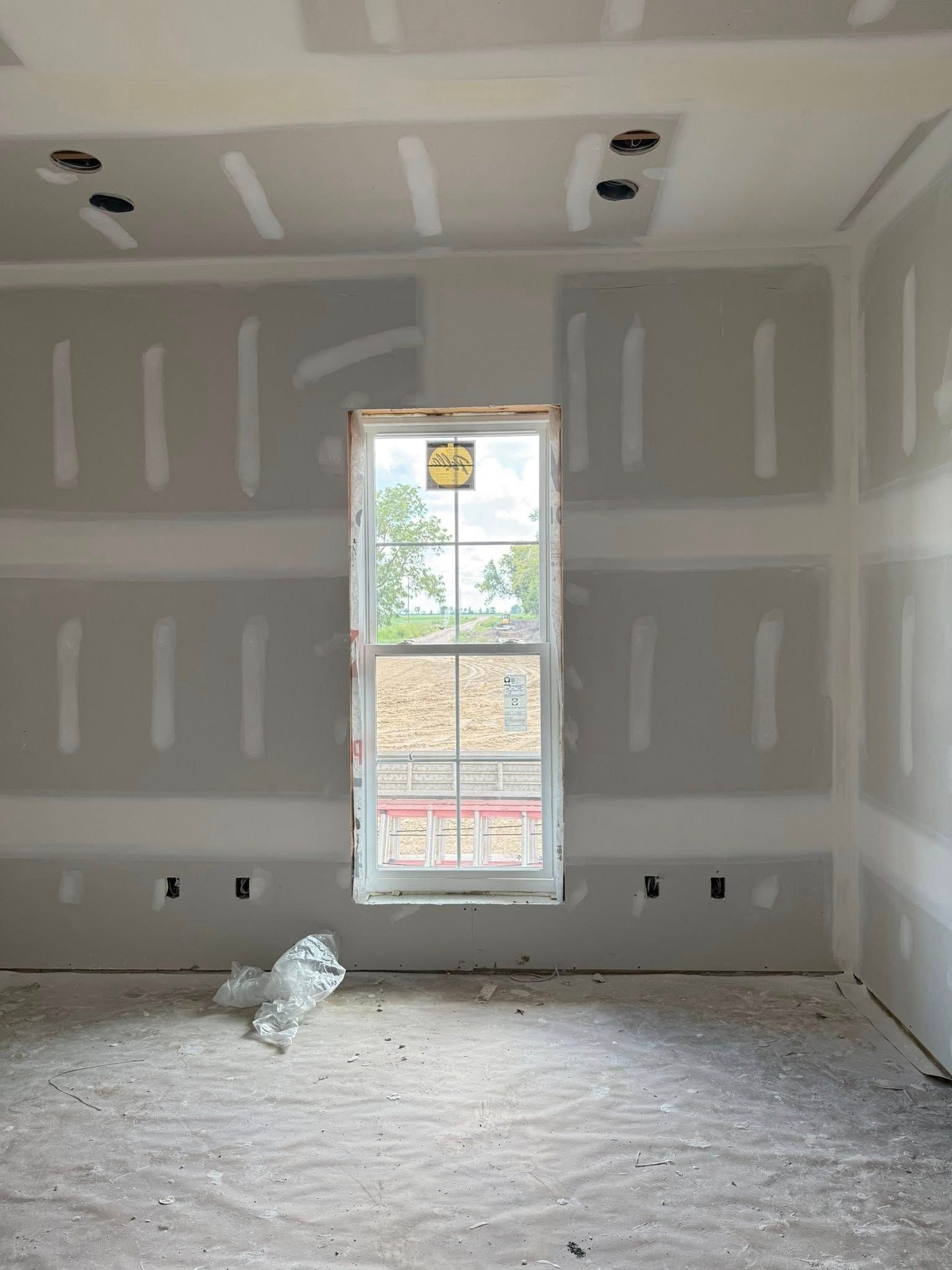 Unfinished room with drywall, a window, and electrical outlets. White and gray with a concrete floor.