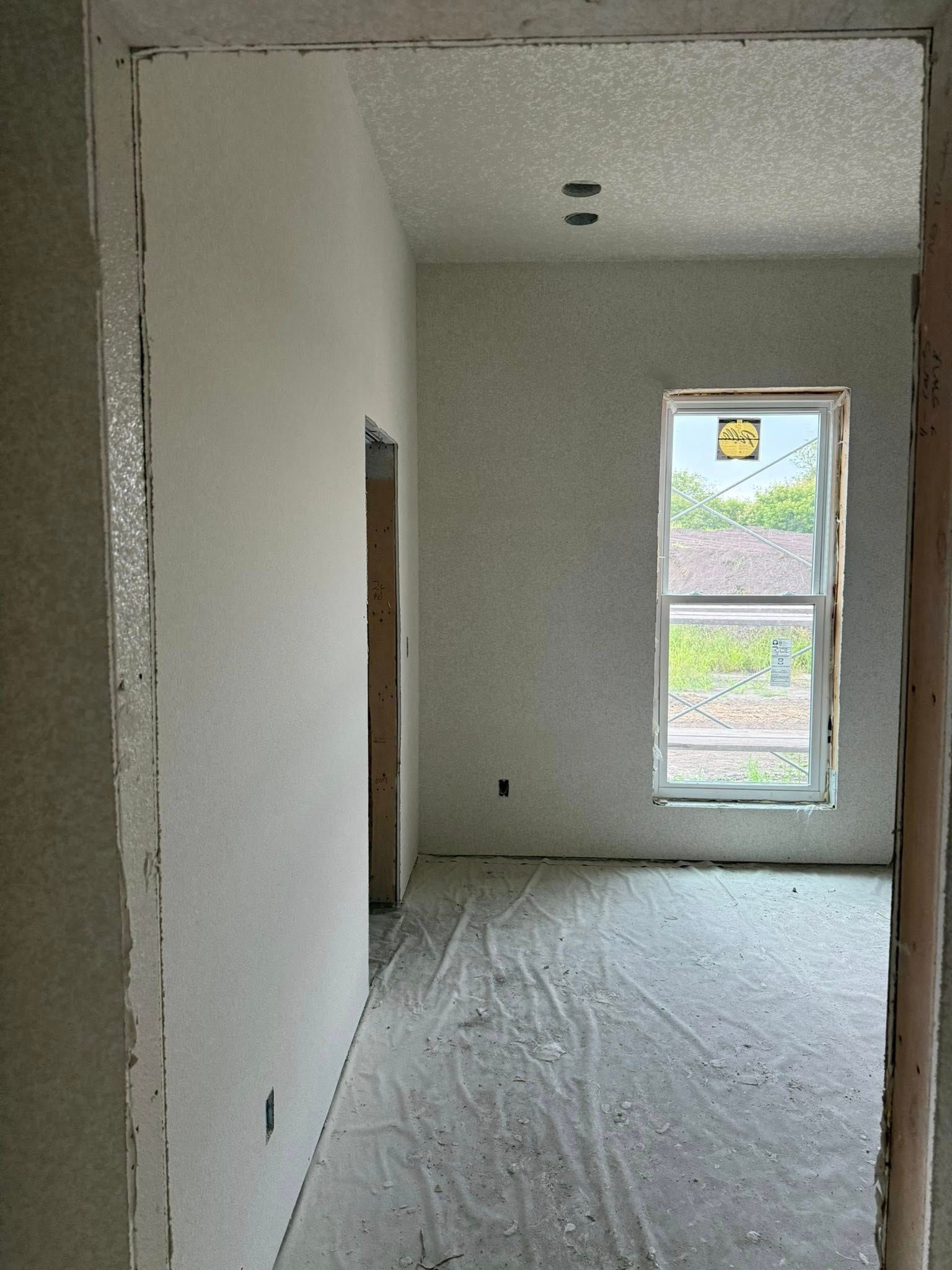 Interior view of a room under construction; bare walls, window, doorway, and unfinished floor.