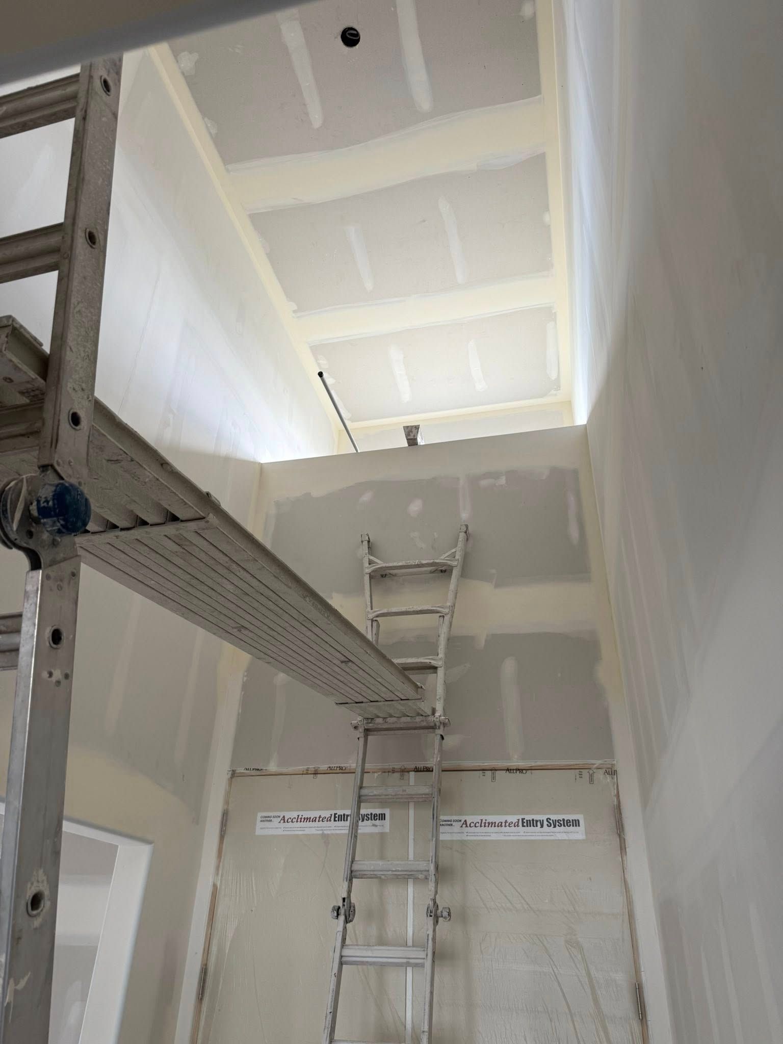 Construction site: drywall installation in progress; scaffold and ladder in a tall, narrow room.