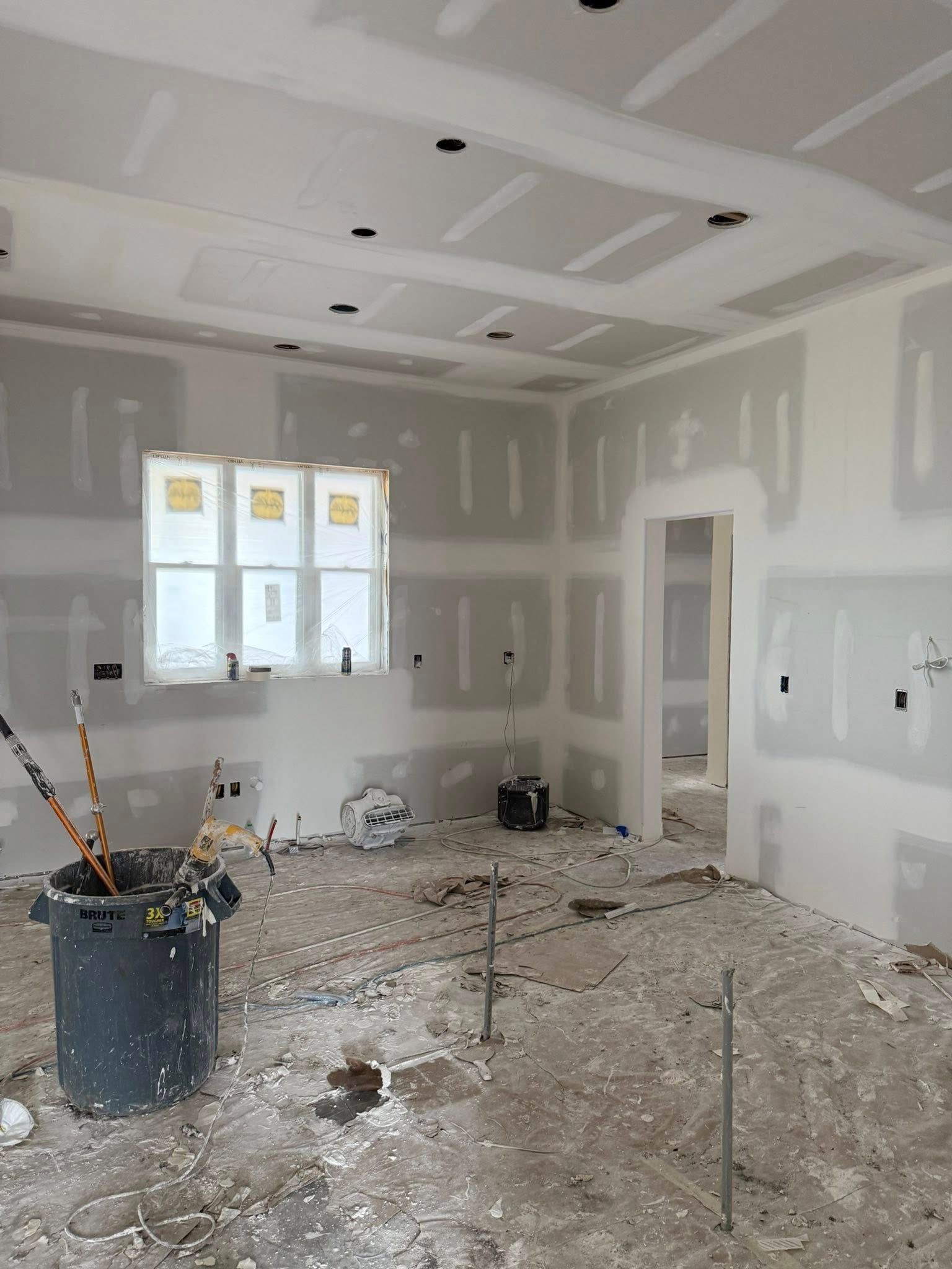 Interior room under construction with drywall installed. Gray walls, white ceiling, and messy floor.