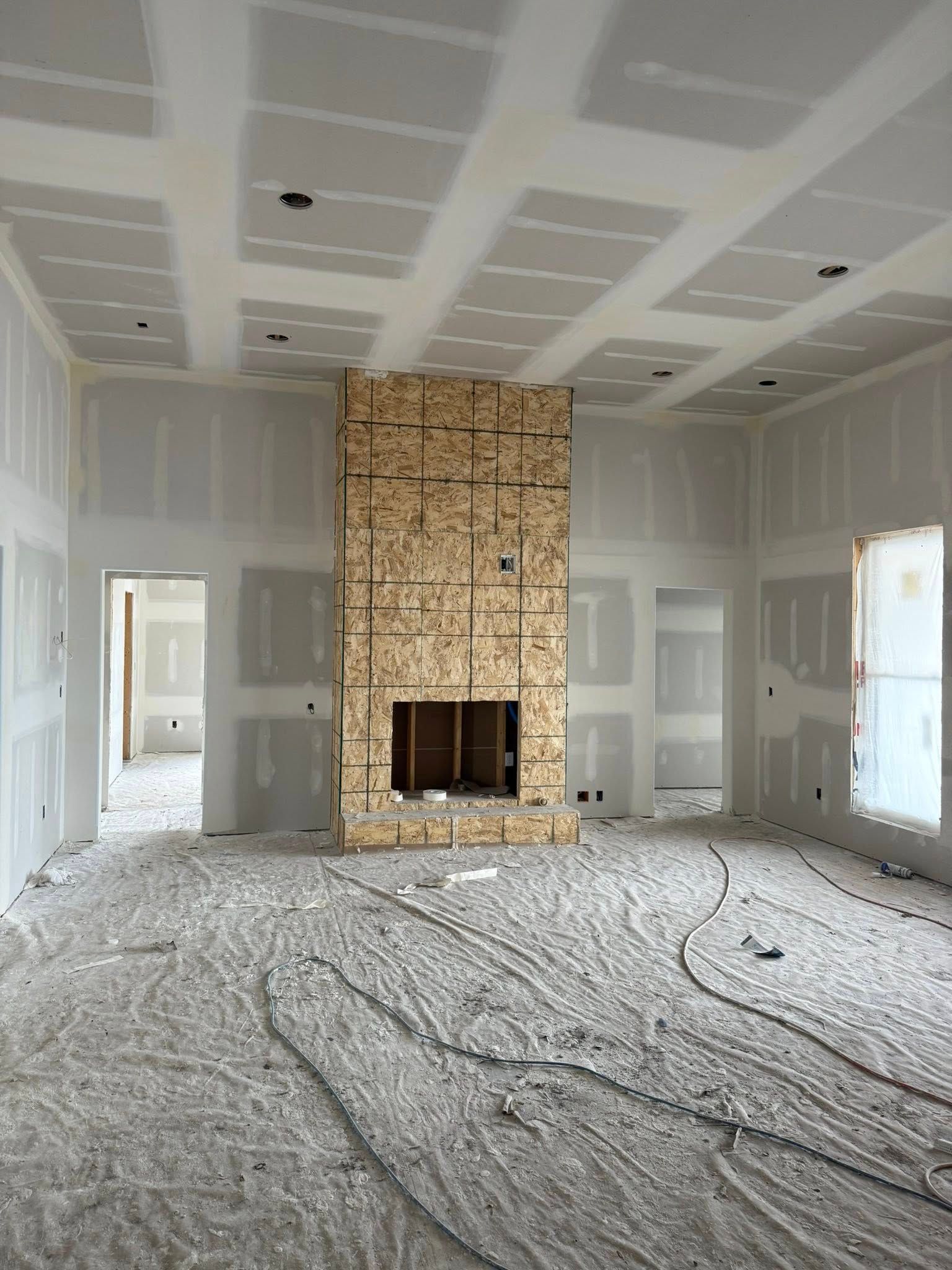 A room under construction with drywall and a wood-framed fireplace, exposed wooden floor.