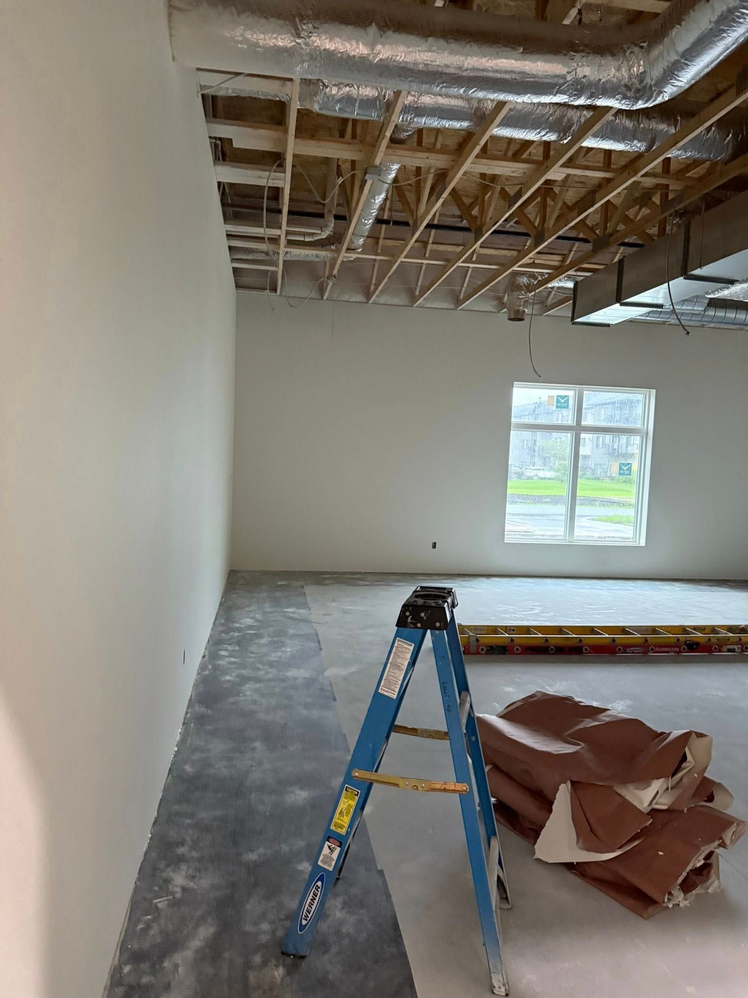 Construction site: room with a window, ladder, exposed ceiling beams, and debris on the floor.