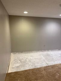 Empty room with gray walls, a concrete floor, and carpeted section; recessed ceiling lights.