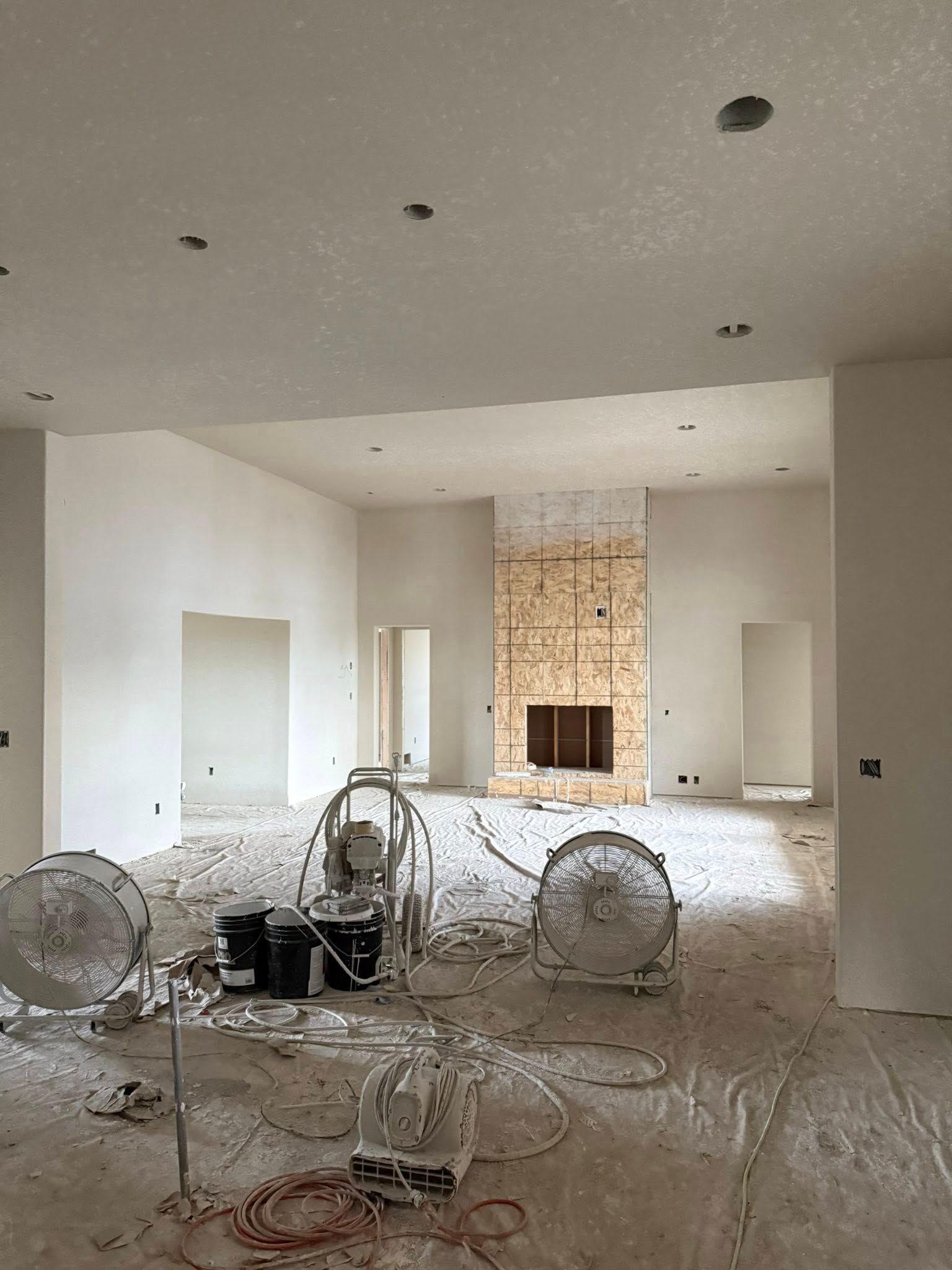 Construction interior with fans, fireplace, and open doorways. Plaster dust covers the floor.