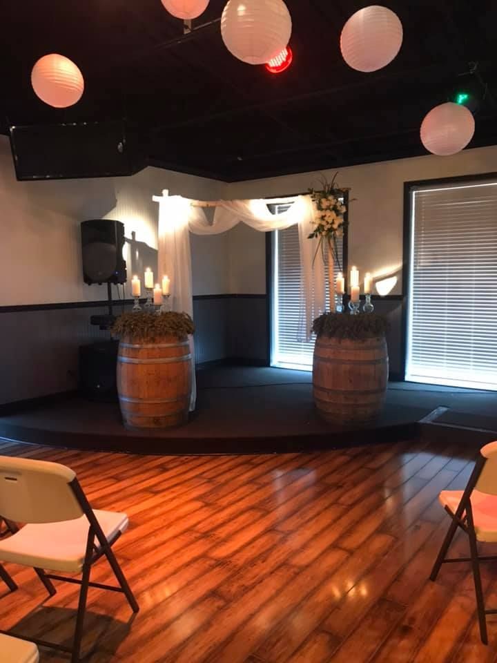A room with wooden floors and chairs and a stage with barrels and candles.