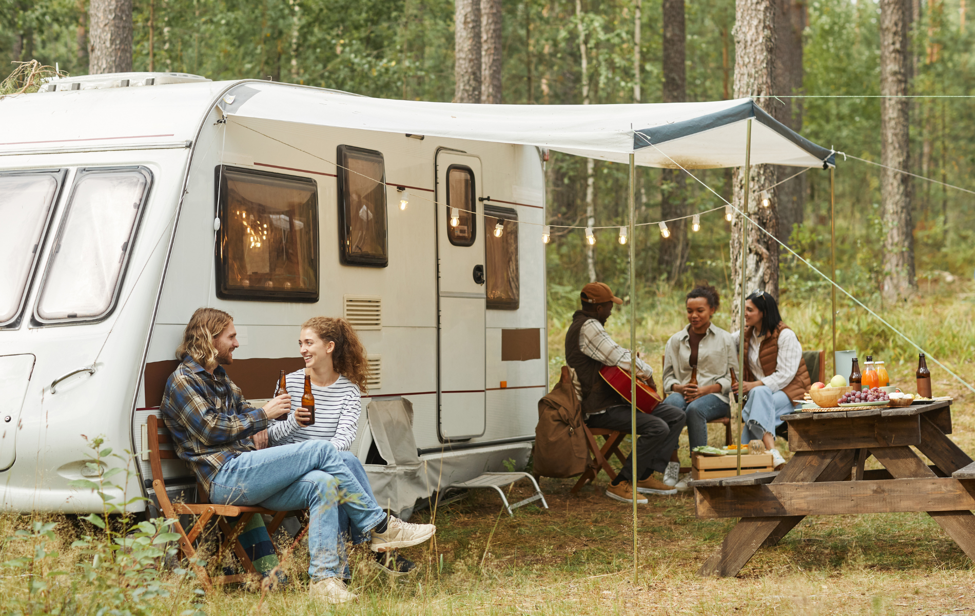 A group of people are sitting at a picnic table in front of a trailer.